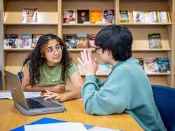 Students talking in library with laptop in front of them